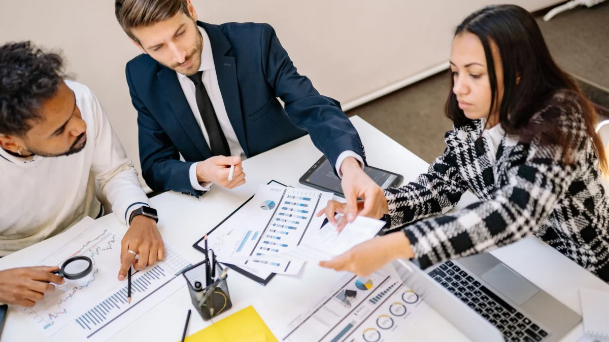 Nhóm đồng nghiệp đối chiếu giấy tờ và máy tính trên bàn